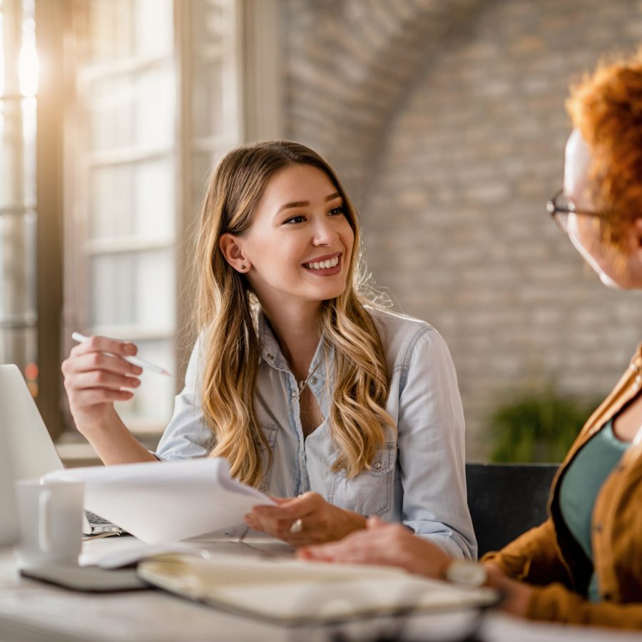 Smiling creative businesswoman going through paperwork and talking to her female colleague in the office.